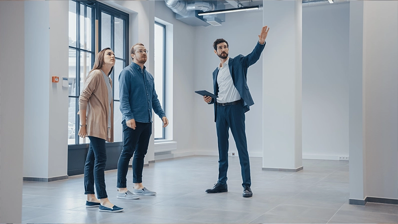 Real Estate Agent Showing a New Empty Office Space to Young Male and Female Hipsters. Entrepreneurs Meet the Broker with a Tablet and Discuss the Facility They Wish to Purchase or Rent.