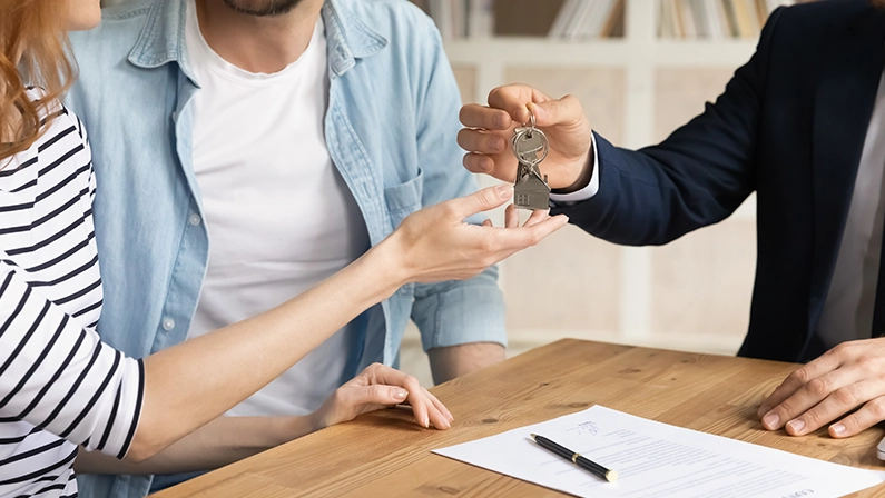 Cropped close up view happy couple receiving keys from new own property, finish meeting in real estate agency lead by realtor in formal suit. Bank mortgage for young family, selling, renting concept