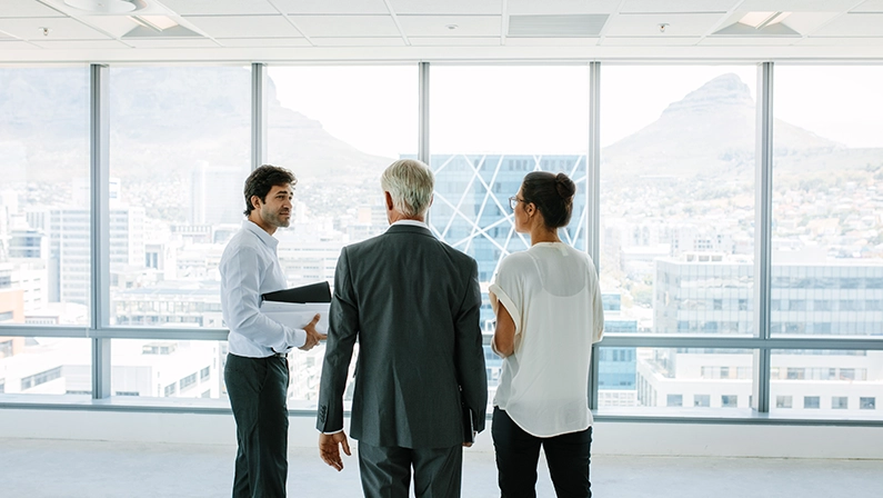 Business people and real estate agent discussing at empty office space. Estate broker talking with potential clients.