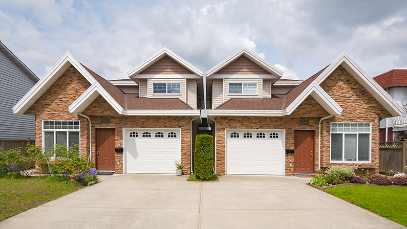 Residential duplex house with concrete drive way and green lawns in front. Two family dwelling with green lawn in front