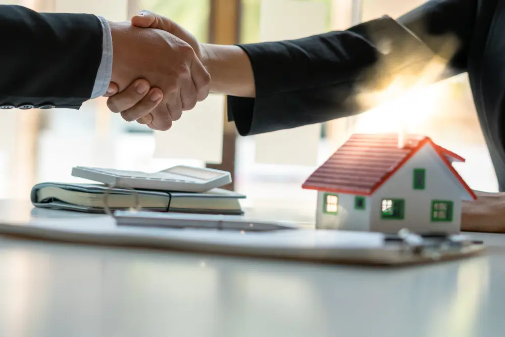 Real estate broker and customer shaking hands after signing a contract: real estate, home loan and insurance concept
