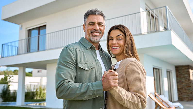 Portrait of happy smiling mature older family couple new property buyers modern dream luxury villa owners standing outside house, affectionate senior middle aged man and woman in love hugging outdoor.