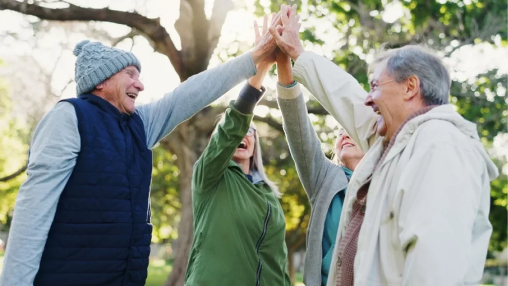 Group of seniors outdoors giving a high five, showing the social activities available in 55 Communities In Houston.