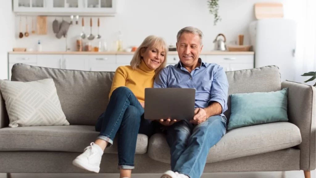 Senior couple sitting on a sofa with a laptop, exploring lifestyle choices and amenities in 55 Communities In Houston.