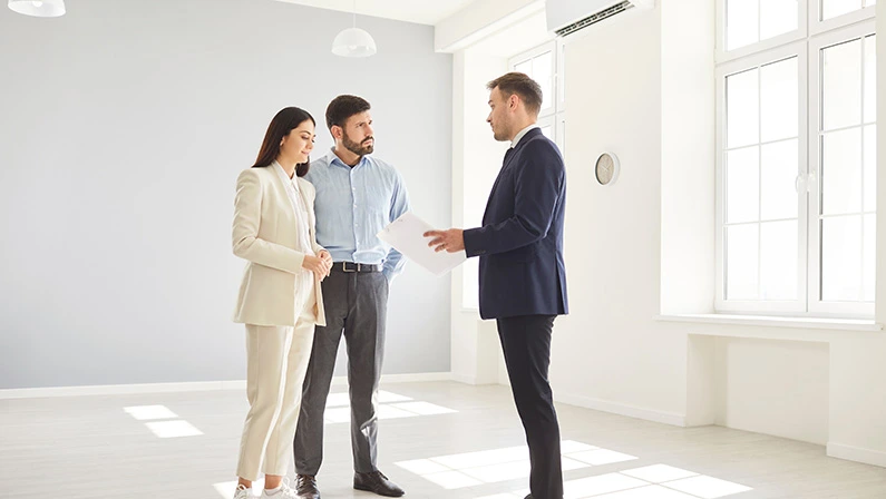 Real estate agent or realtor guides a clients couple through a new home, introducing them to the property prior to purchase or rent. Agent helping clients make an informed decision.