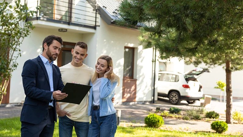 Real estate agent presenting clipboard with documents to couple in front of residential property